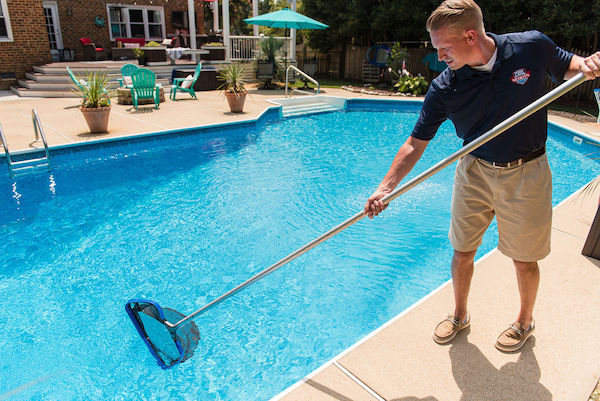 Pool technician skimming pool water in customer's backyard