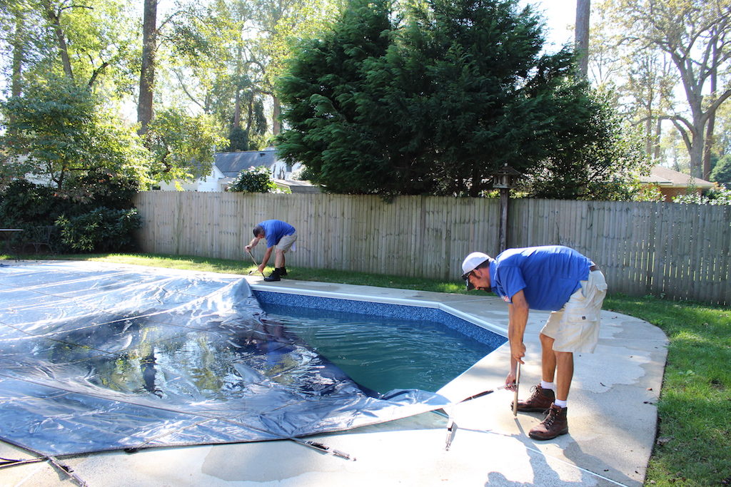 Two Pool Scouts technicians putting a cover on a swimming pool in a backyard