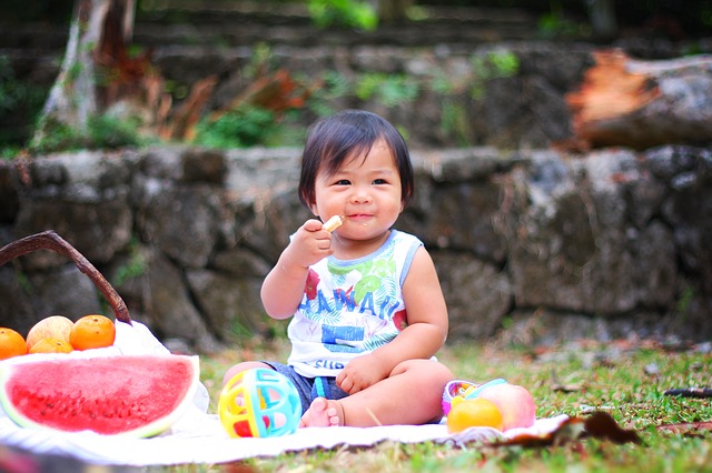 Little girl eating while sitting on a picnic blanket with toys
