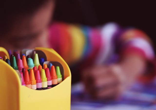 Box of crayons with child coloring in background