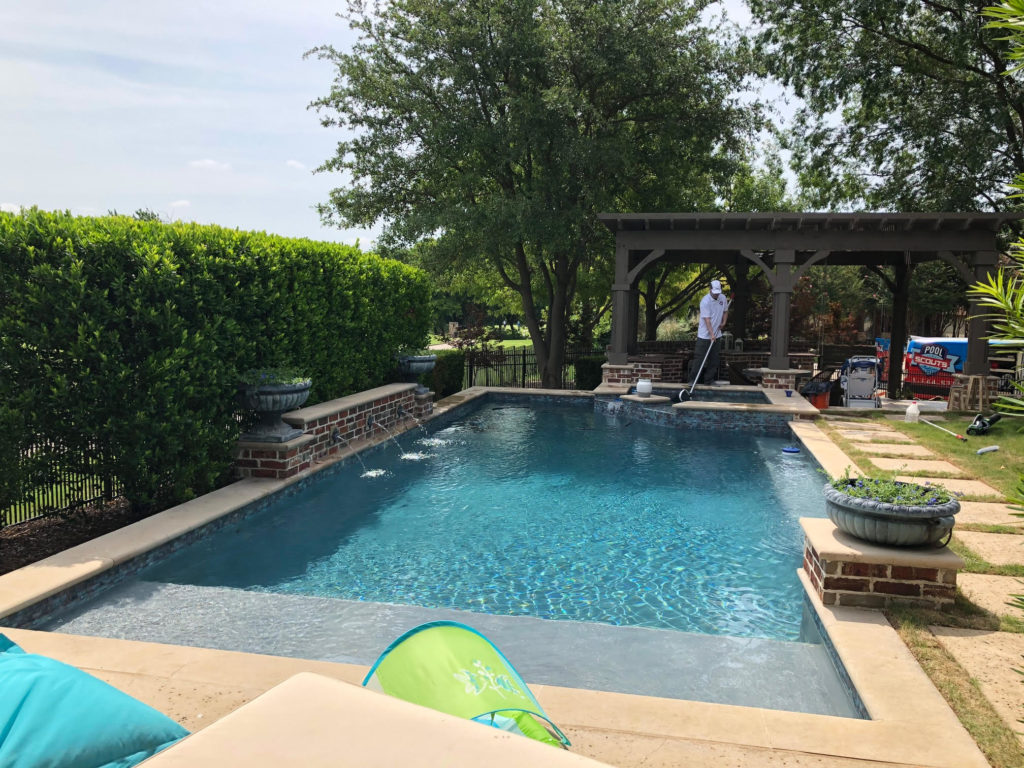 Swimming pool in backyard in Texas, with person using a pool net to clean it