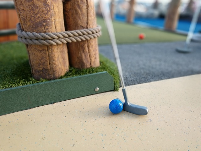 Close up view of mini golf putter and ball next to green turf