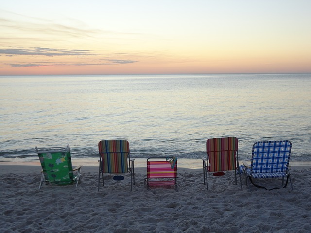 Beach chairs lined up in sand overlooking sunset