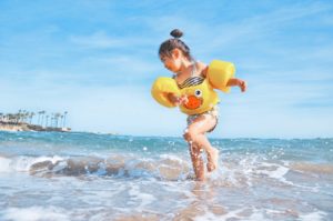 Little girl running in the water at the beach laughing, with floaties on 