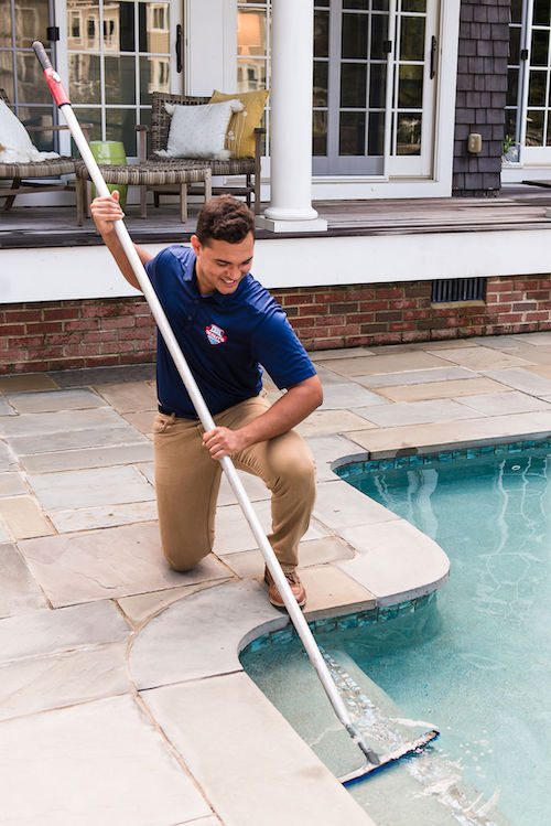 Pool Scouts technician kneeling and sweeping top step of swimming pool