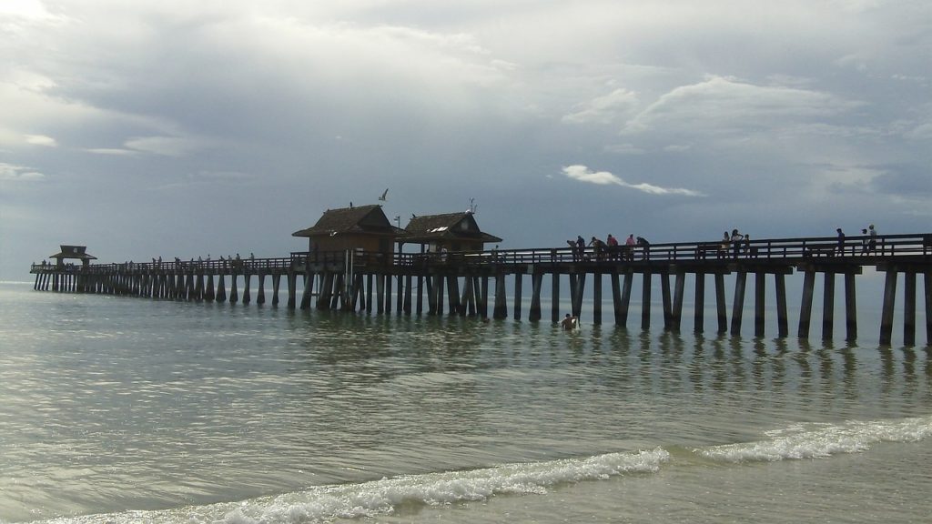 Pier on the beach with people walking and fishing in Naples, FL