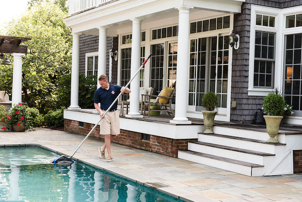 Pool tech using net to skim leaves from a swimming pool