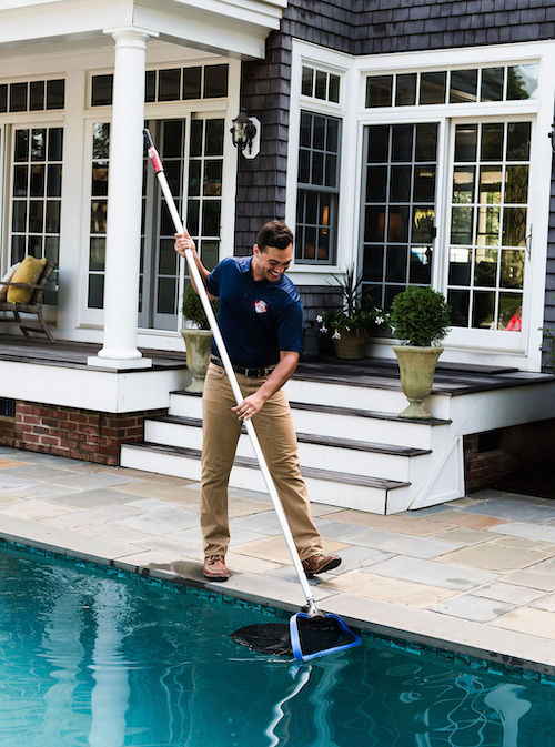 Pool Scouts technician skimming a swimming pool in customer's backyard
