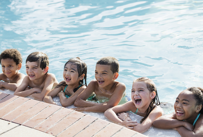 Happy kids smiling along the edge of a clean swimming pool