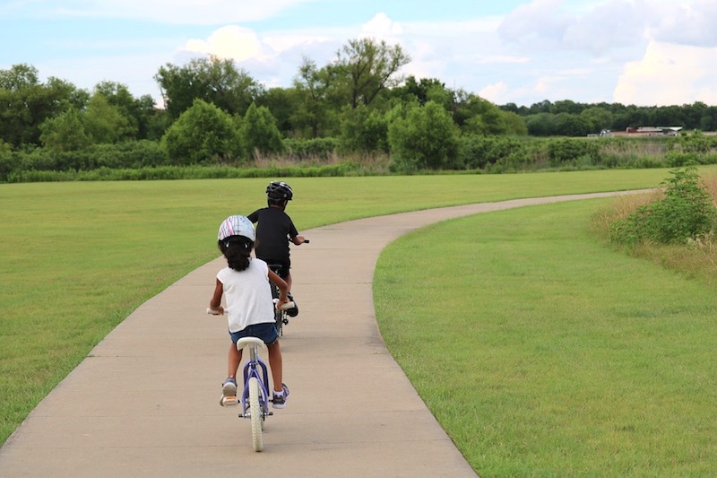 Two kids bike riding on a path in the park