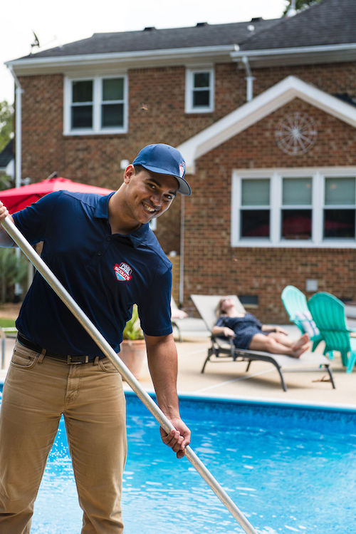 Pool technician cleaning pool while customer relaxes by pool