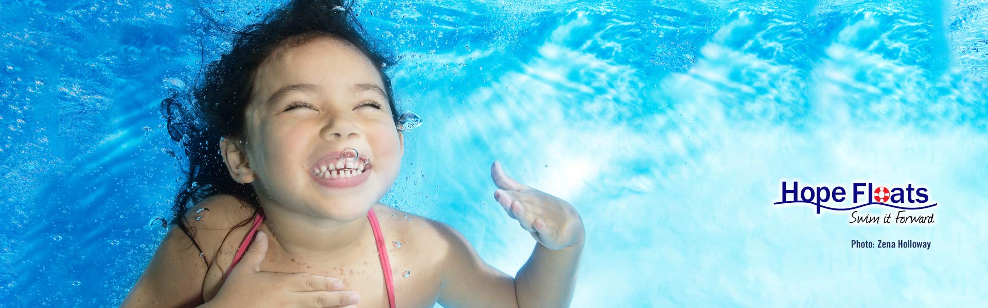 Little girl smiling underwater after receiving swim lessons from Hope Floats Foundation