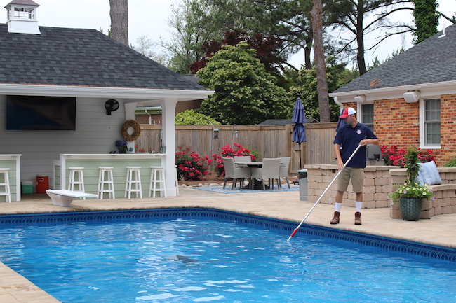 Pool Technician skimming leaves out of a pool during pool service