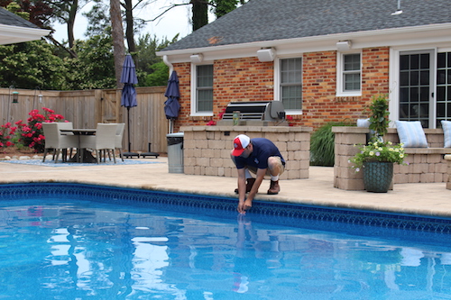 Pool technician bent down next to swimming pool testing pool water chemical levels