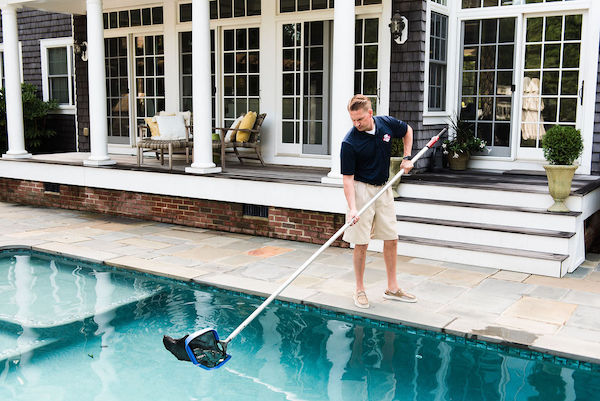 Pool Scouts tech using pool net to skim debris from swimming pool