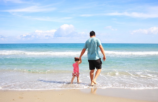 Father and daughter holding hands along the seashore at the beach on a sunny day
