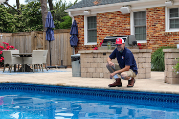 Pool technician kneeling next to a clean pool
