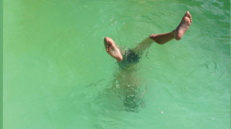 Person doing handstand in a dirty green pool
