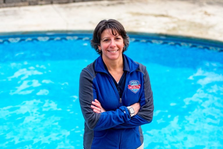 Pool Scouts owner Tiffiny standing in front of a pool and smiling with arms crossed