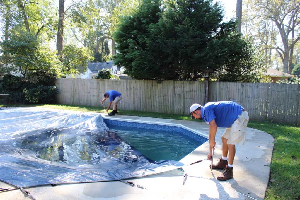 Two pool technicians putting a pool cover on a swimming pool