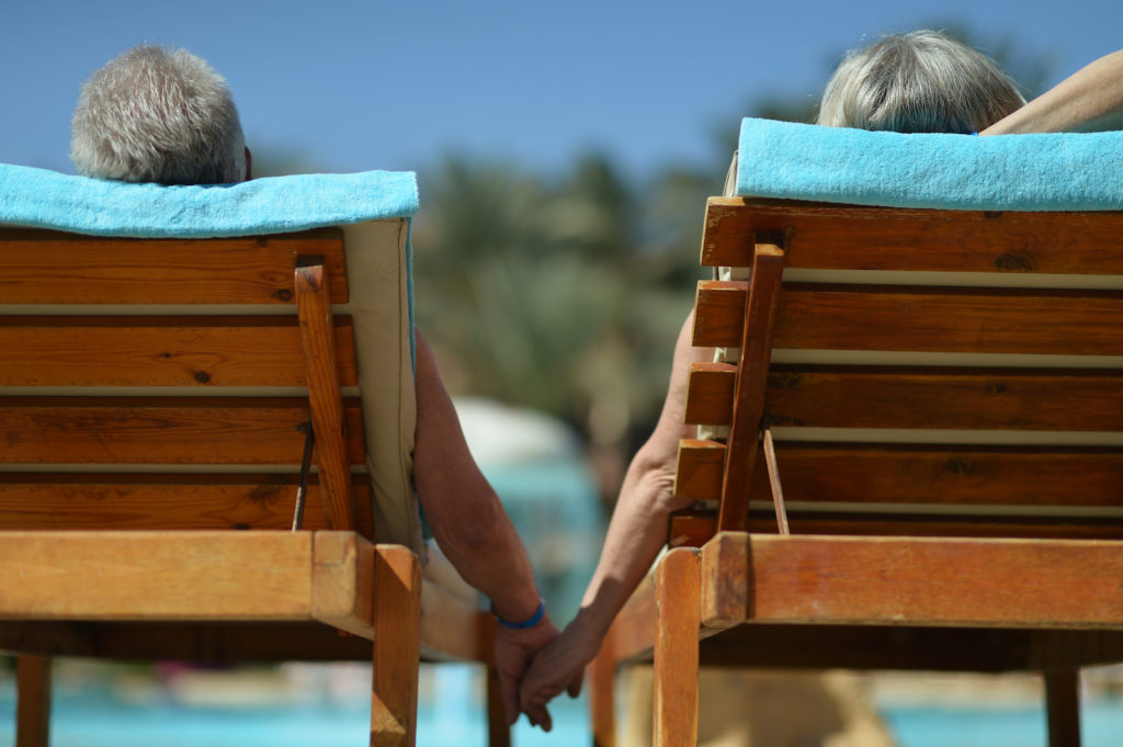 Back view of Elderly couple lying by pool at hotel resort